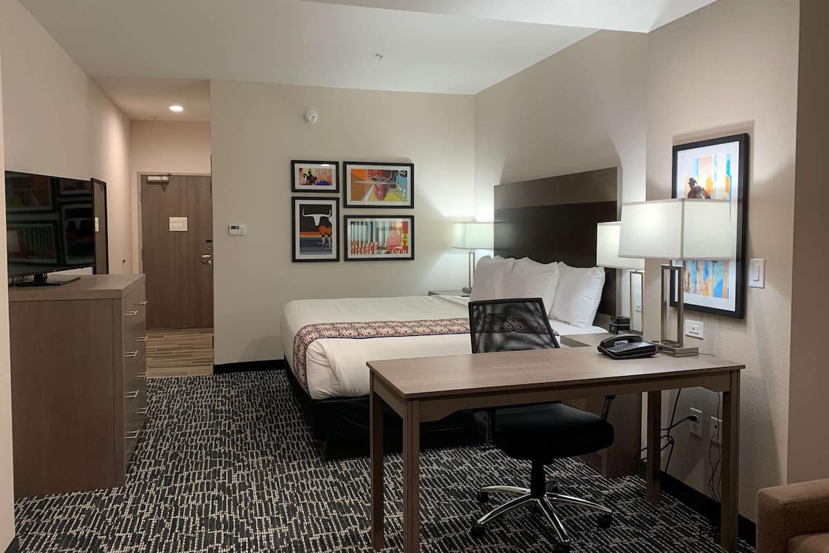 A hotel room with a bed, desk, chair, and a TV on a cabinet.