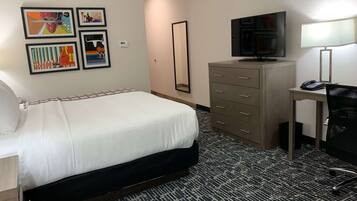 A hotel room with a bed, a desk with a chair, a television, a mirror, and artwork on the wall.