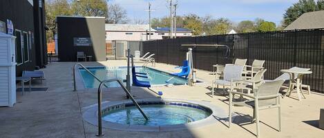 A pool area with a hot tub, lounge chairs, and a small table.