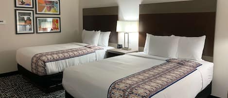 Une chambre d’hôtel avec deux lits, une tête de lit, une table de chevet, une lampe et quatre tableaux encadrés accrochés au mur.