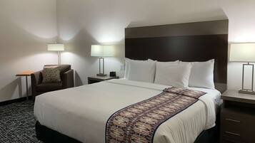 Una habitación de hotel con una cama grande, dos mesitas de noche, una silla y dos lámparas.