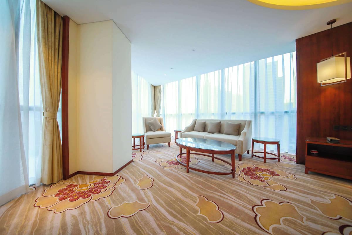 A hotel room with a large window, two sofas, a coffee table, and a wooden cabinet.