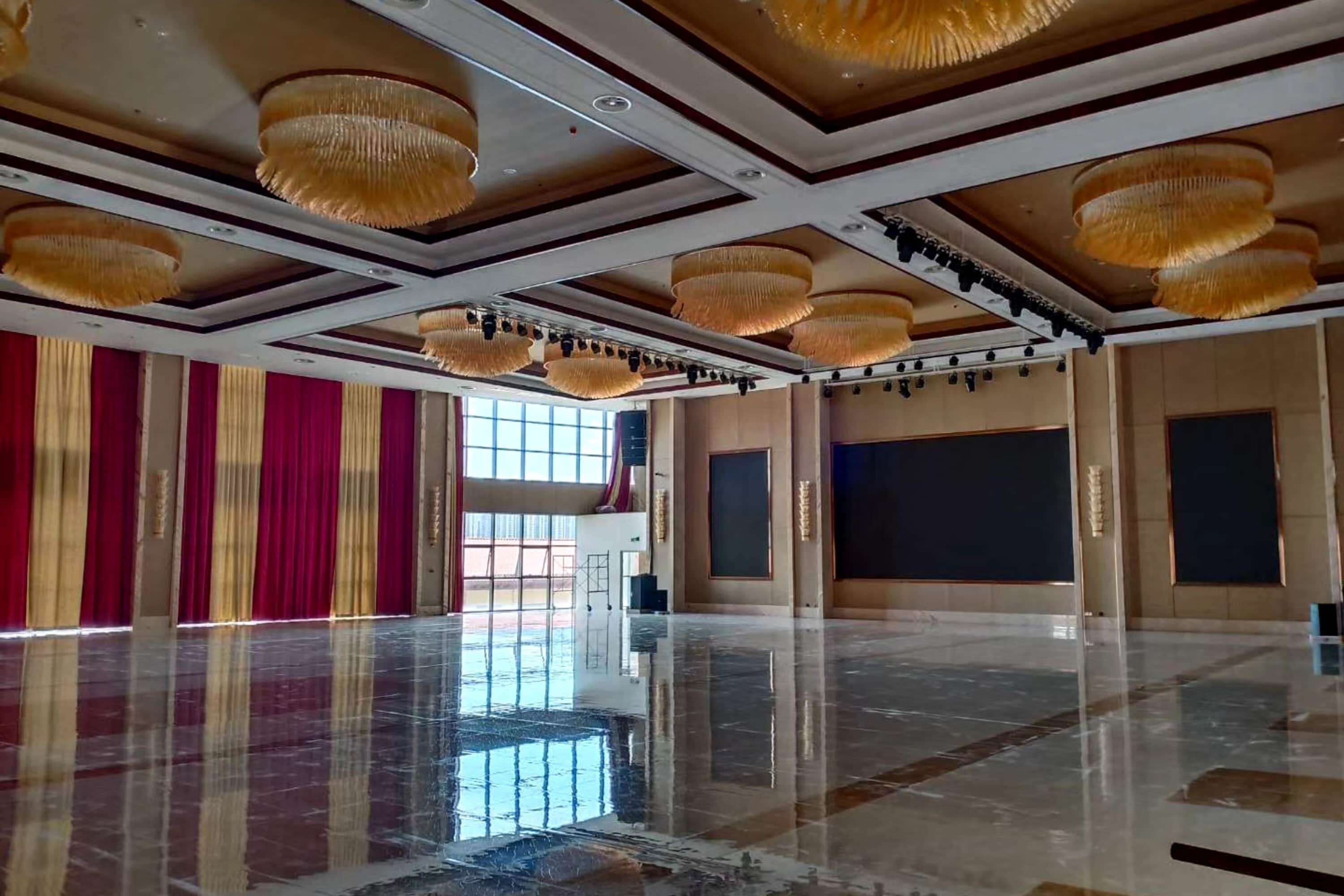 A spacious hall with a polished marble floor, large chandeliers, and red curtains.