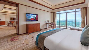 Une chambre d’hôtel avec un grand lit, un téléviseur fixé au mur, un bureau et une vue sur la ville grâce à de grandes fenêtres.