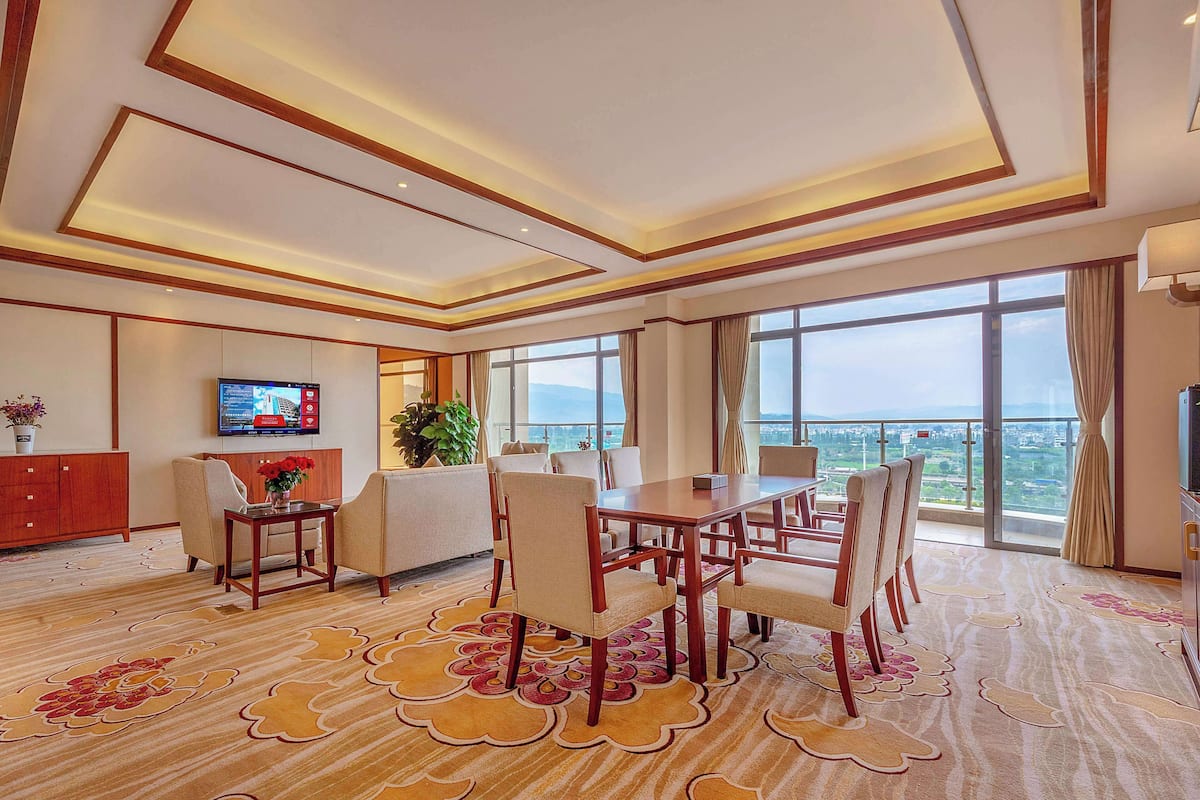 A spacious room with a dining area, a television mounted on the wall, and large windows offering a view of the cityscape.