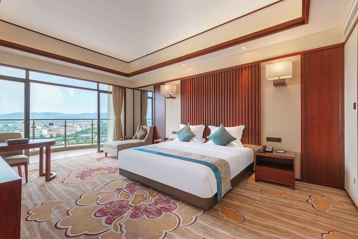 A hotel room with a large bed, a desk, a chair, and a view of the city.