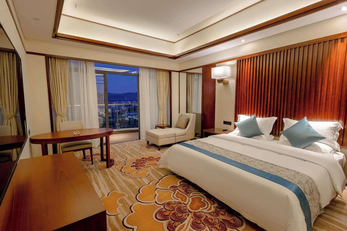 A hotel room with a large bed, a desk, a chair, and a view of the cityscape.
