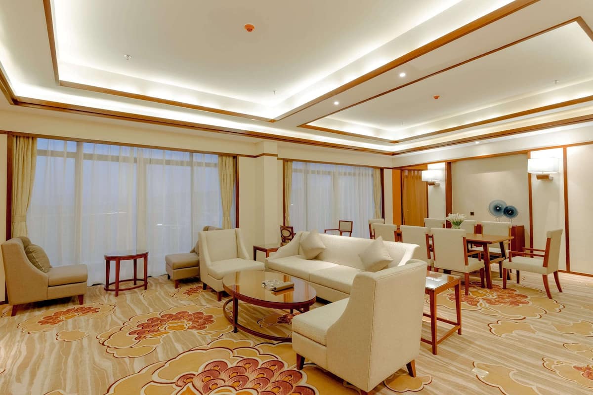 A spacious hotel room with a large sofa set, a coffee table, and a dining area with chairs and a table.