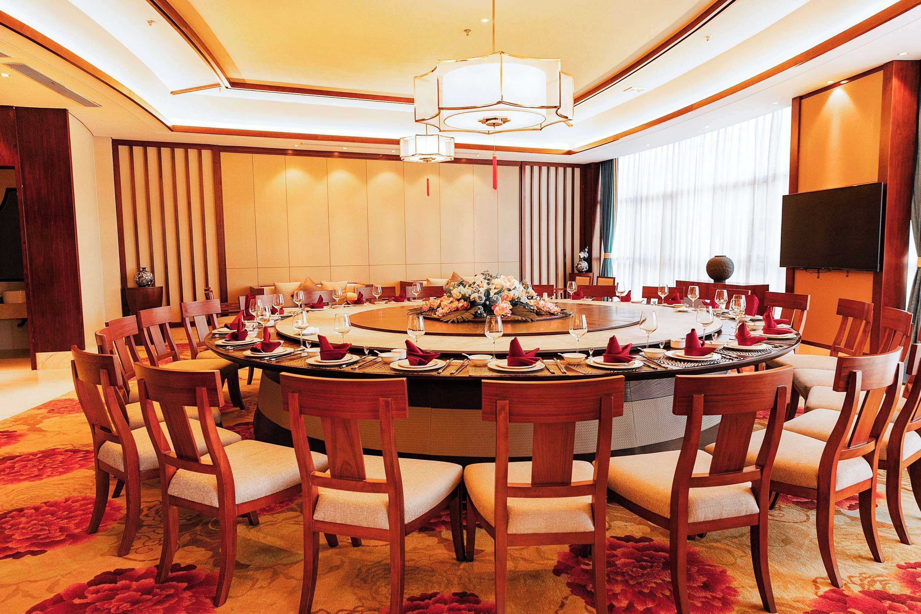A conference room with a round table, wooden chairs, and a chandelier.