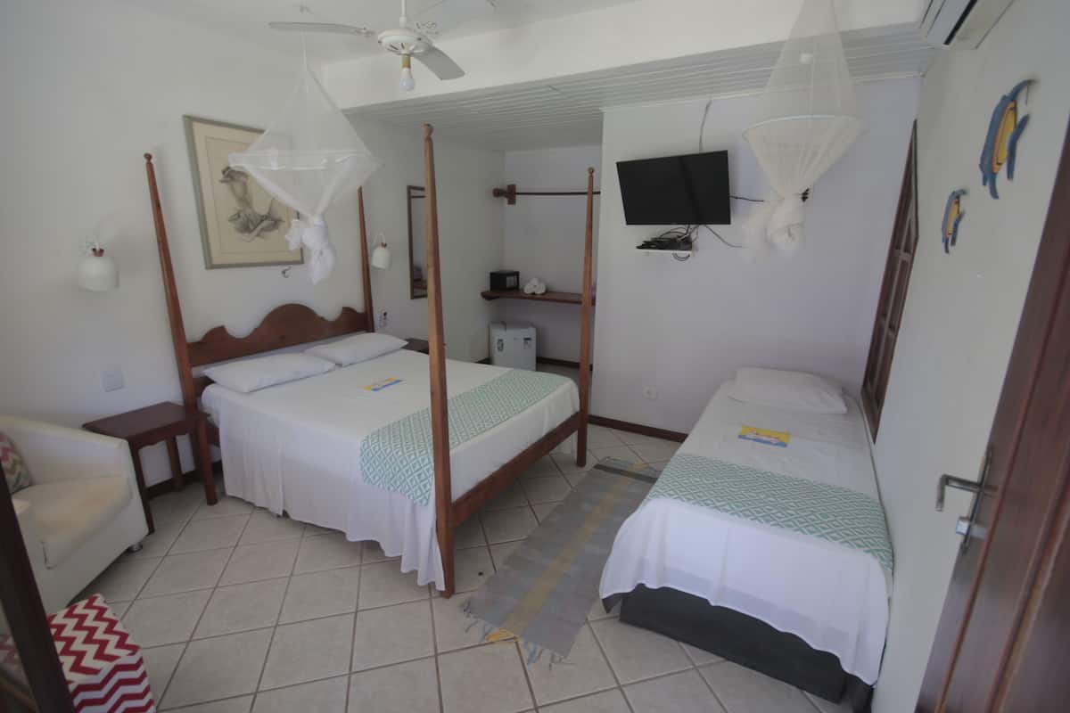 A room with two single beds, a ceiling fan, a TV mounted on the wall, and a mosquito net over one bed.