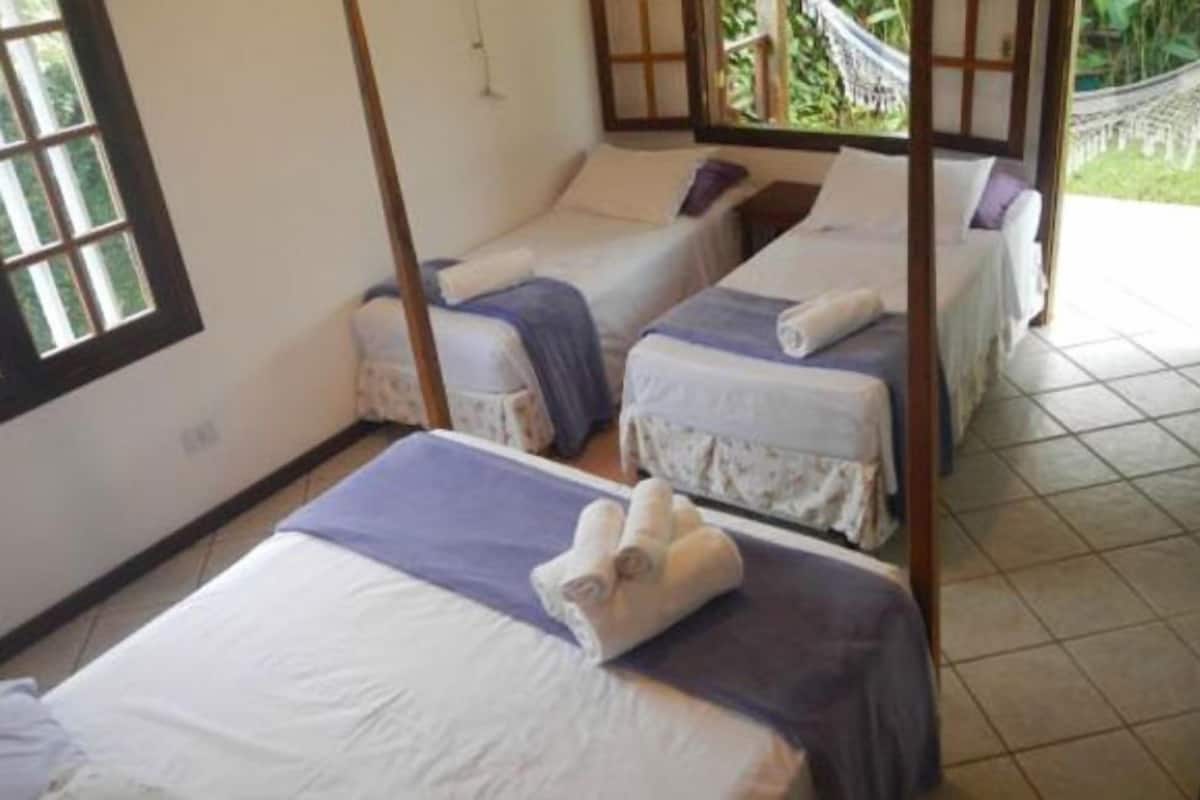 A room with two single beds, each with a wooden frame and a purple bedspread. There is a window on the left side of the room.