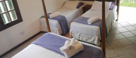 A room with two single beds, each with a wooden frame and a purple bedspread. There is a window on the left side of the room.