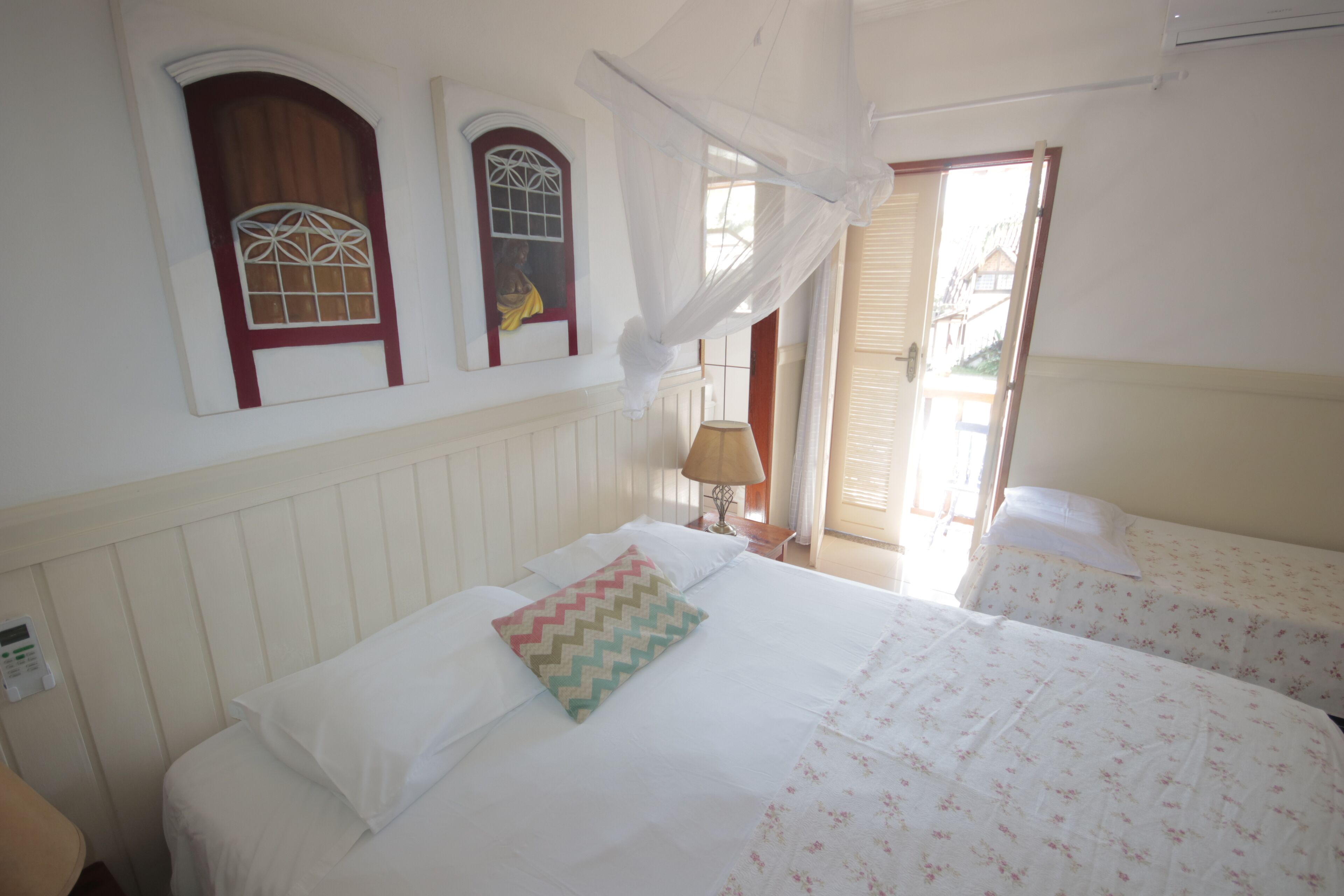 A hotel room with a bed, a bedside table with a lamp, and a window with a decorative grille.