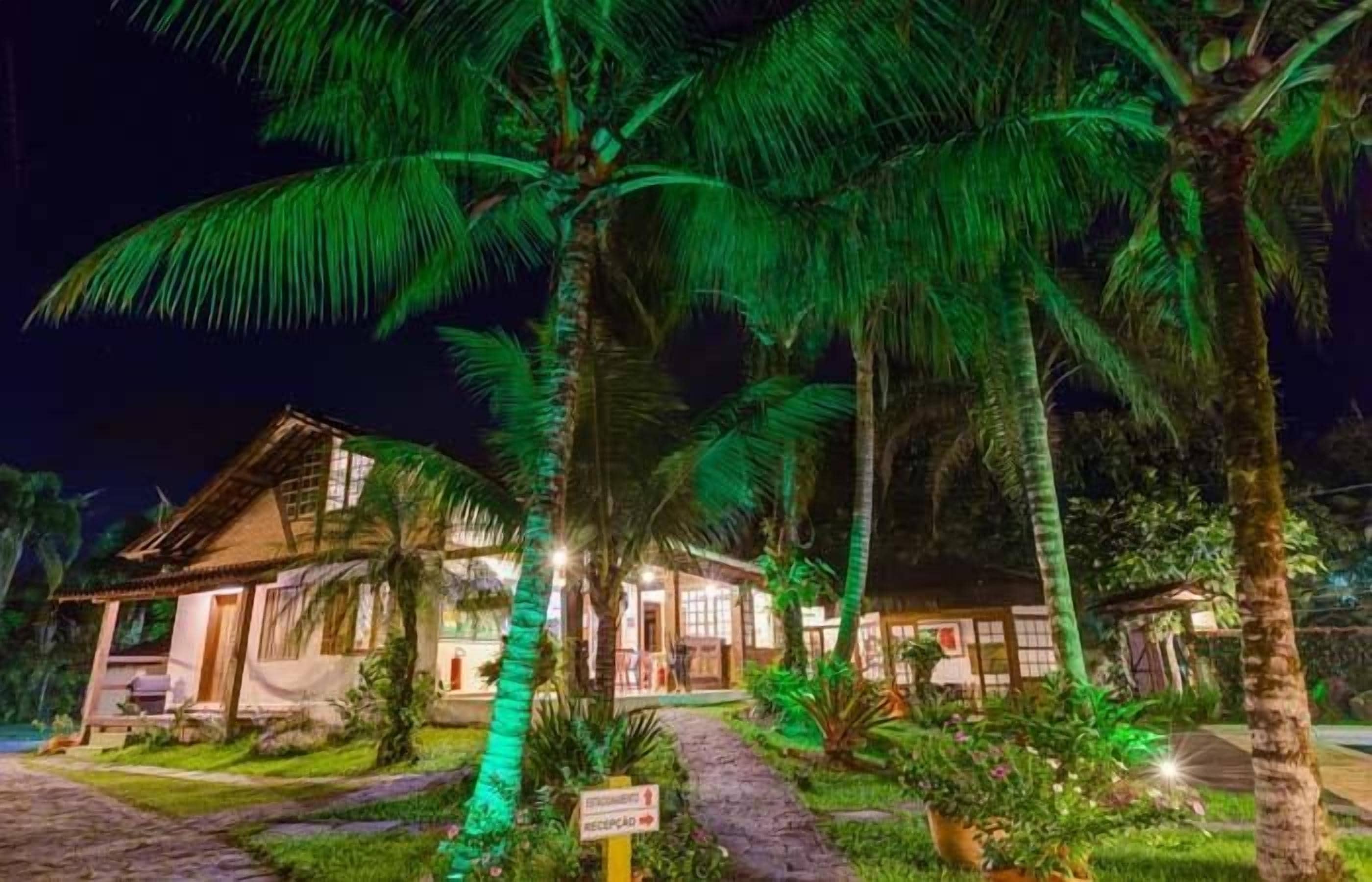 A well-lit resort with a traditional wooden building, surrounded by palm trees and a paved pathway.