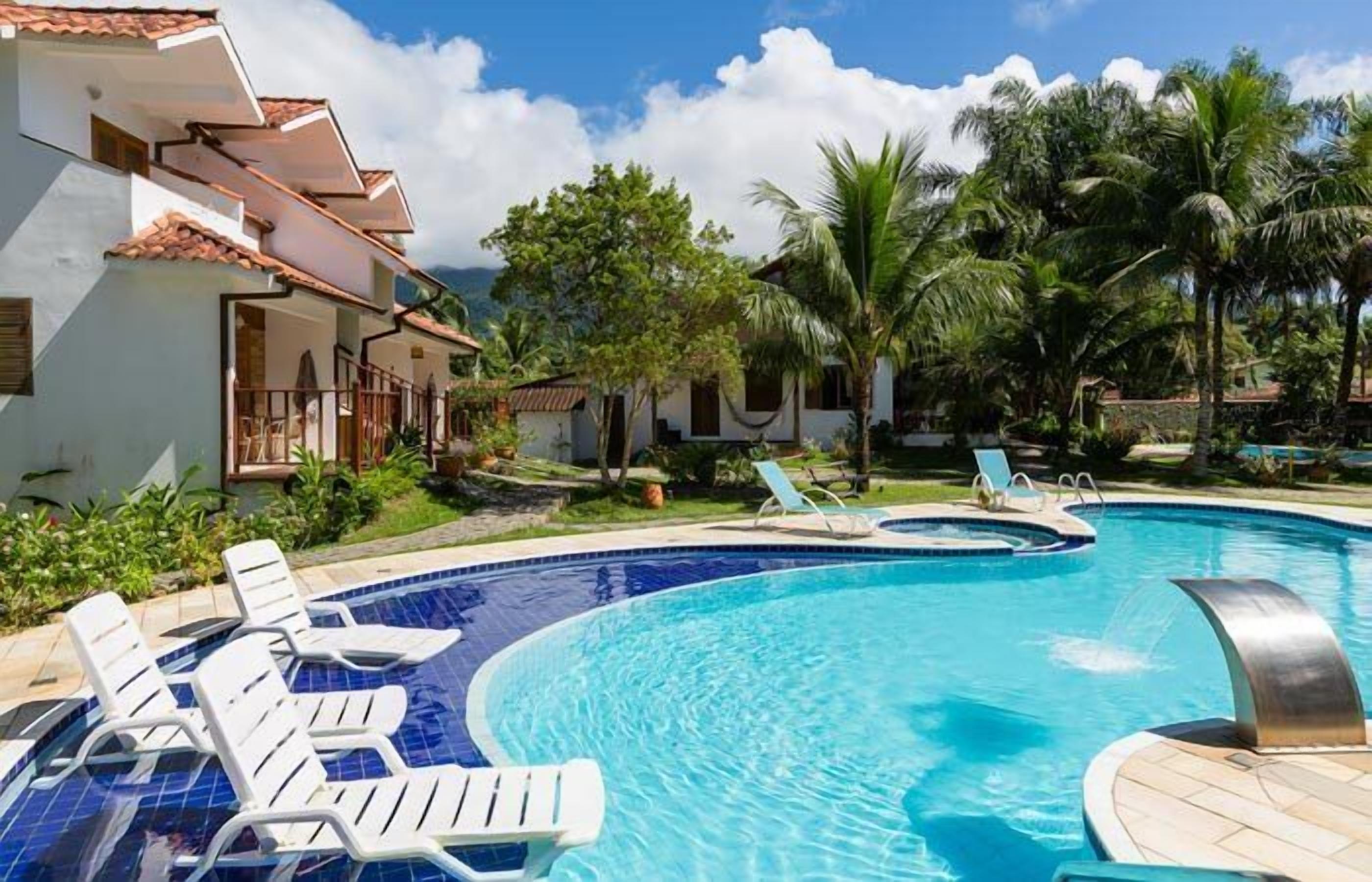 A swimming pool with lounge chairs, surrounded by palm trees and a building with a tiled roof.