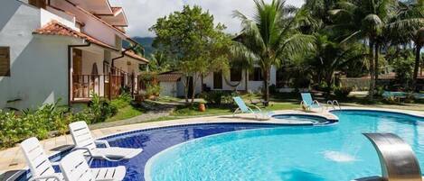 A swimming pool with lounge chairs, surrounded by palm trees and a building with a tiled roof.