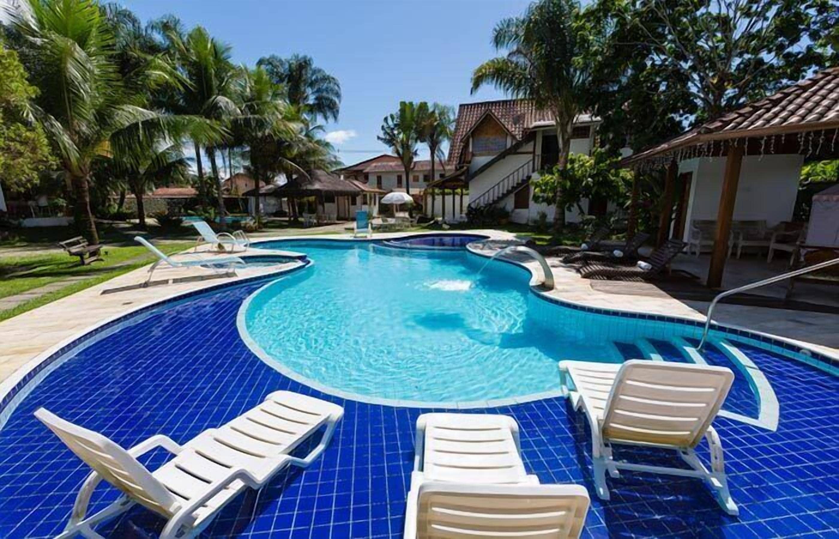 A circular pool with blue tiles, surrounded by lounge chairs and palm trees.