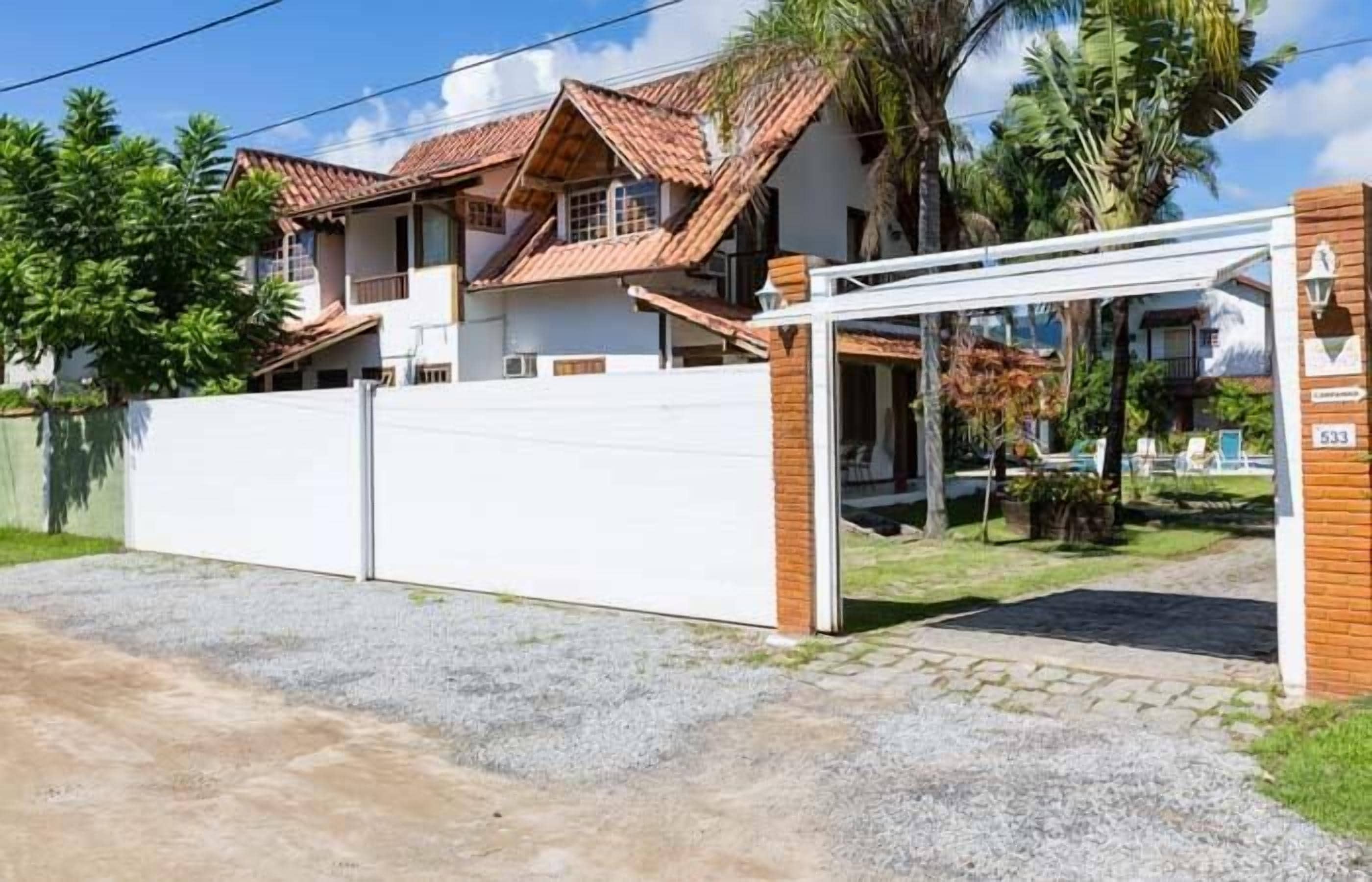 A two-story house with a tiled roof, a gated entrance, and a covered outdoor area with chairs.