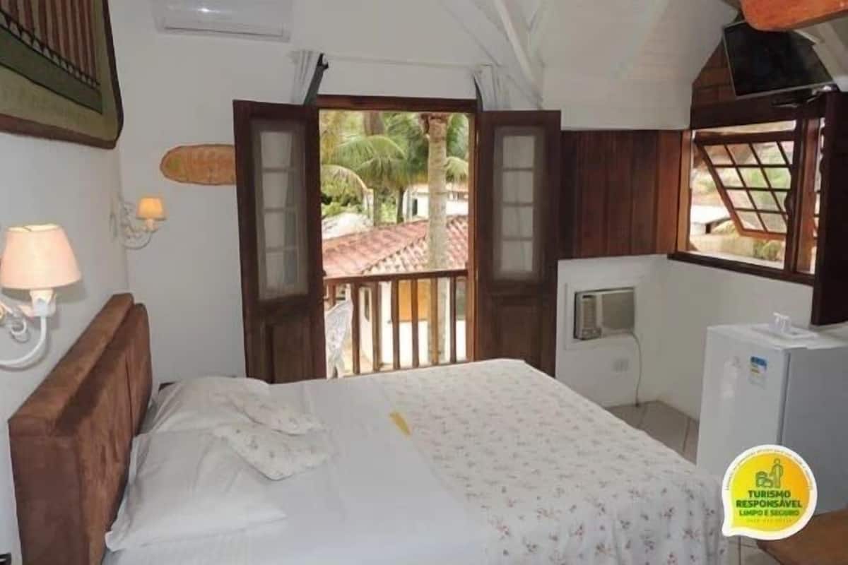 A room with a bed, a window, a lamp, and a refrigerator.