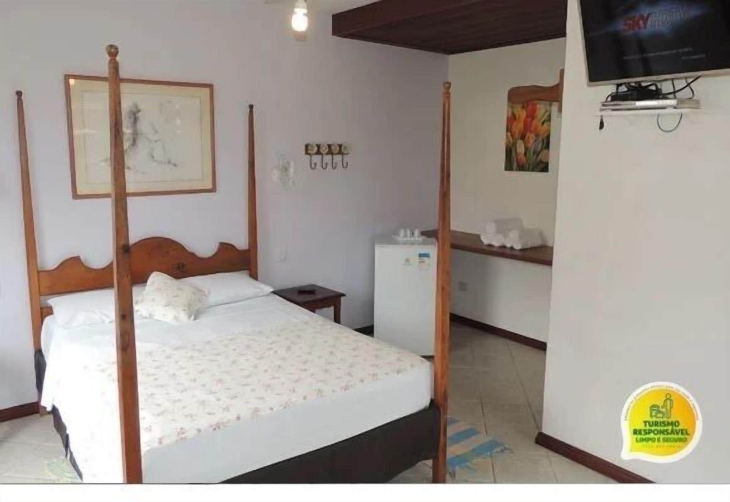 A bedroom with a four-poster bed, a small bedside table, a wall-mounted TV, and a painting.