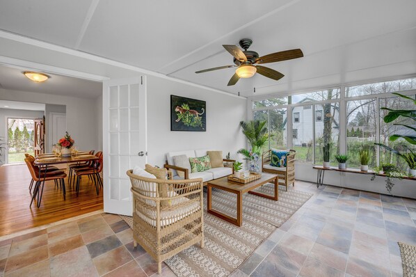 A spacious living room with a dining area, large windows, and a ceiling fan.