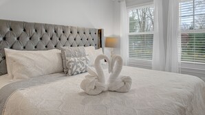 Quarto com cabeceira estofada, cama com colcha estampada e arranjo decorativo de almofadas em formato de cisne.