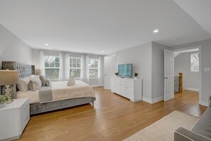 Un dormitorio con cama, cómoda, televisor y una puerta que da a otra habitación.