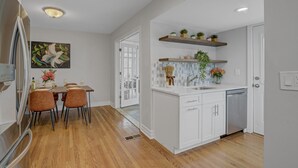 Cozinha moderna com armários brancos, máquina de lavar louça embutida e área de jantar com mesa e cadeiras.