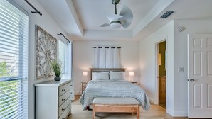 Une chambre à coucher comprenant un lit, des lampes de chevet, un ventilateur de plafond, une commode et une fenêtre avec des stores.