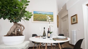 A dining area with a round table, chairs, a potted plant, a wine bottle, and a framed painting on the wall. - SAN GIOVANNI APARTMENT 80 SQM (Roma)