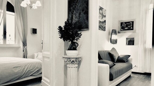 A modern living room with a bed, a sofa, a potted plant, and artwork on the walls. - SAN GIOVANNI APARTMENT 80 SQM (Roma)