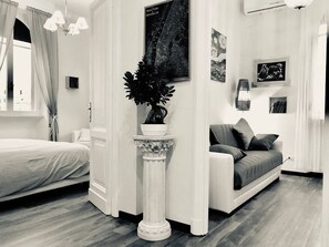 A modern living room with a bed, a sofa, a potted plant, and artwork on the walls.