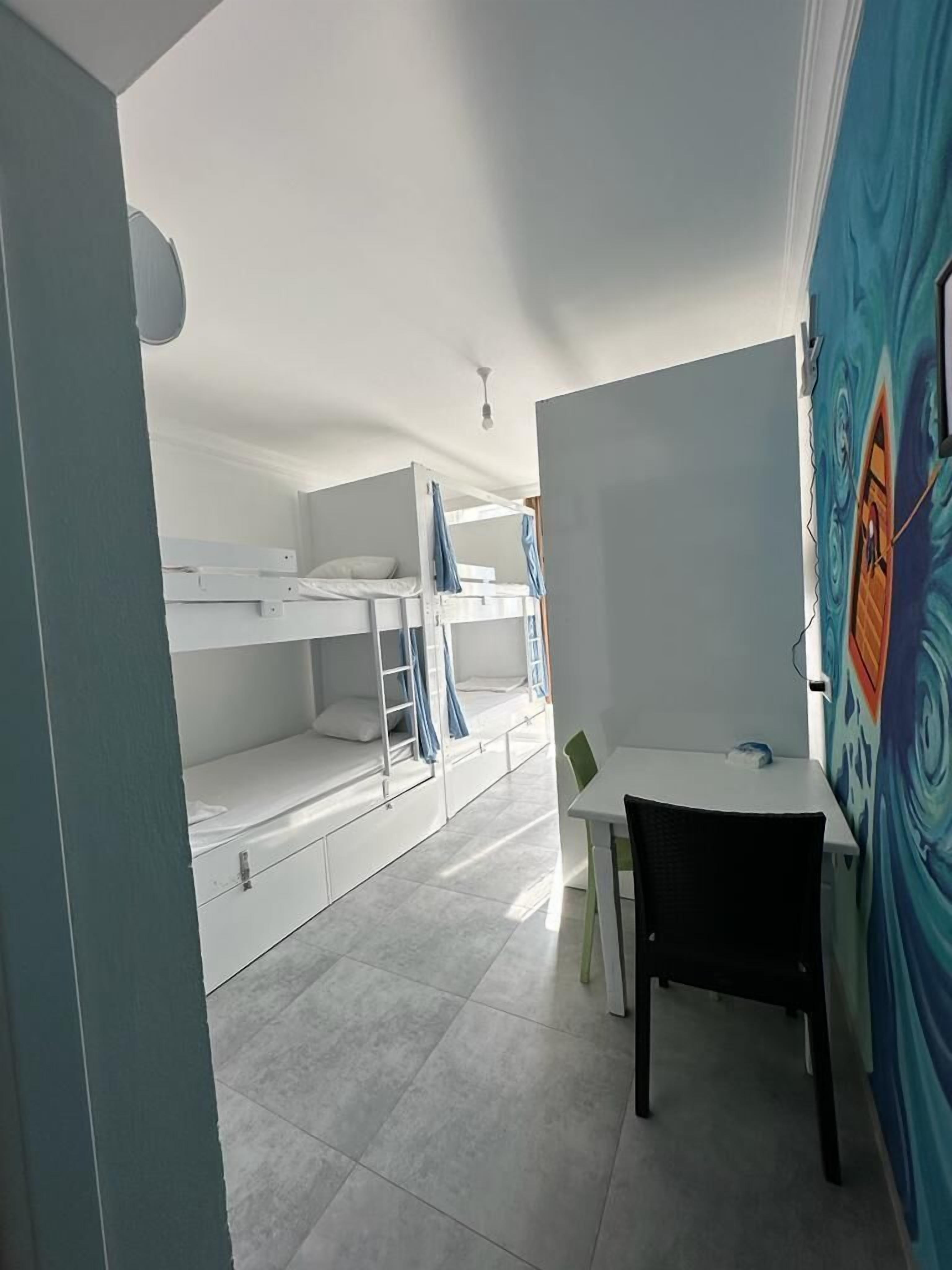 A dormitory room with bunk beds, a desk, and a chair.