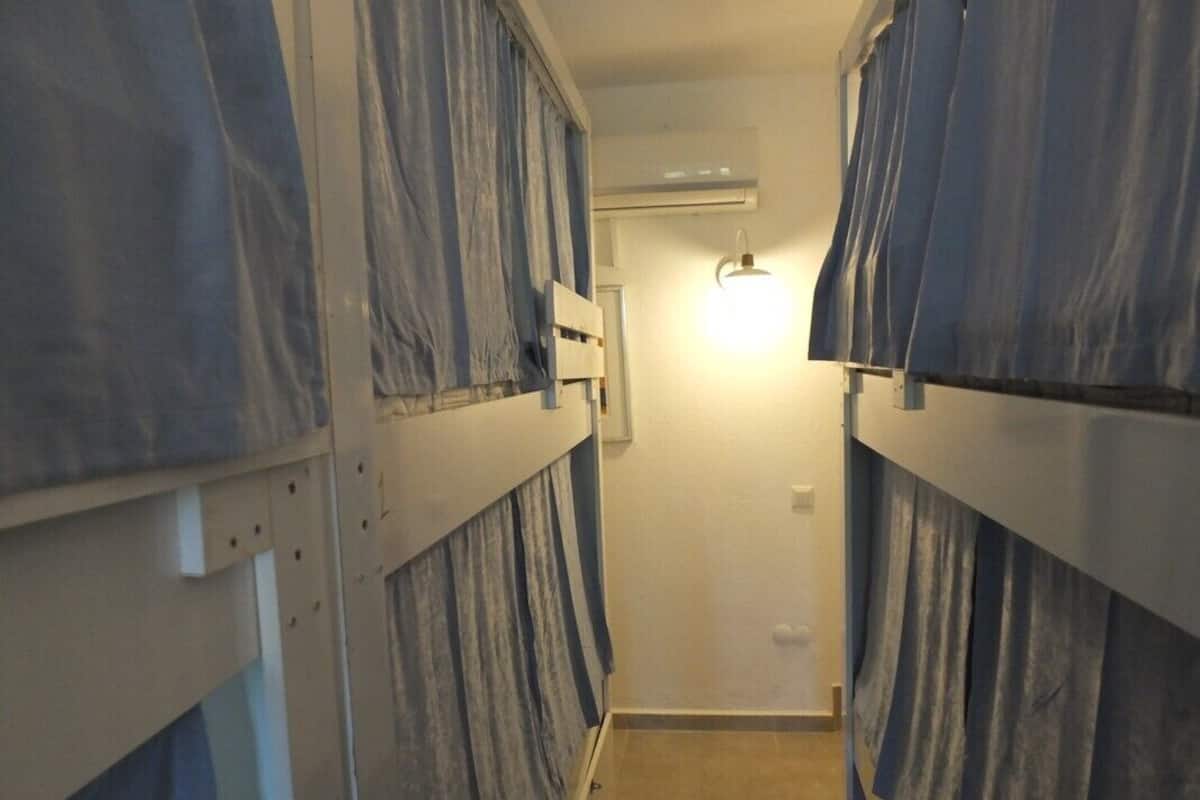 A narrow corridor with bunk beds on either side, a light fixture on the wall, and a door at the end.