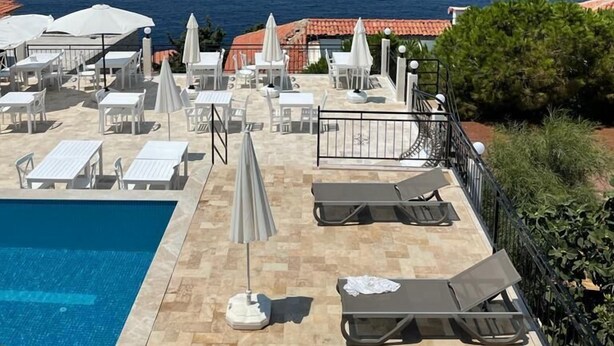 A poolside area with lounge chairs and umbrellas, overlooking a body of water and a distant coastline. - Sole'n Blu Hotel (Kas)