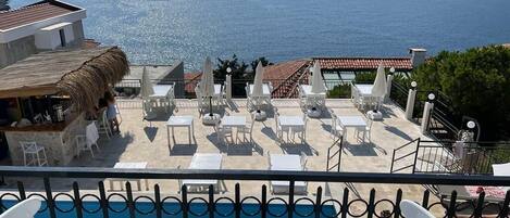 A poolside area with lounge chairs and tables, overlooking a body of water and distant land.