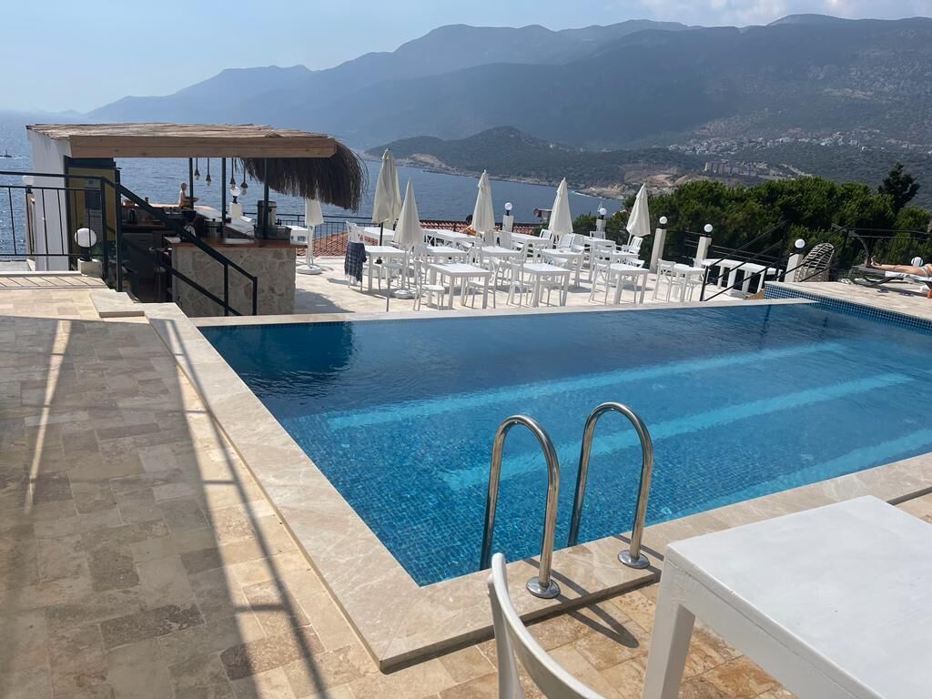 A pool area with a bar, lounge chairs, and a view of the sea and mountains.