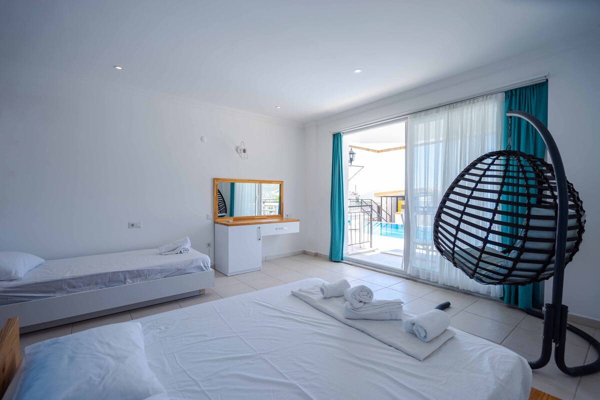 A hotel room with two beds, a desk, a mirror, and a large window with curtains.
