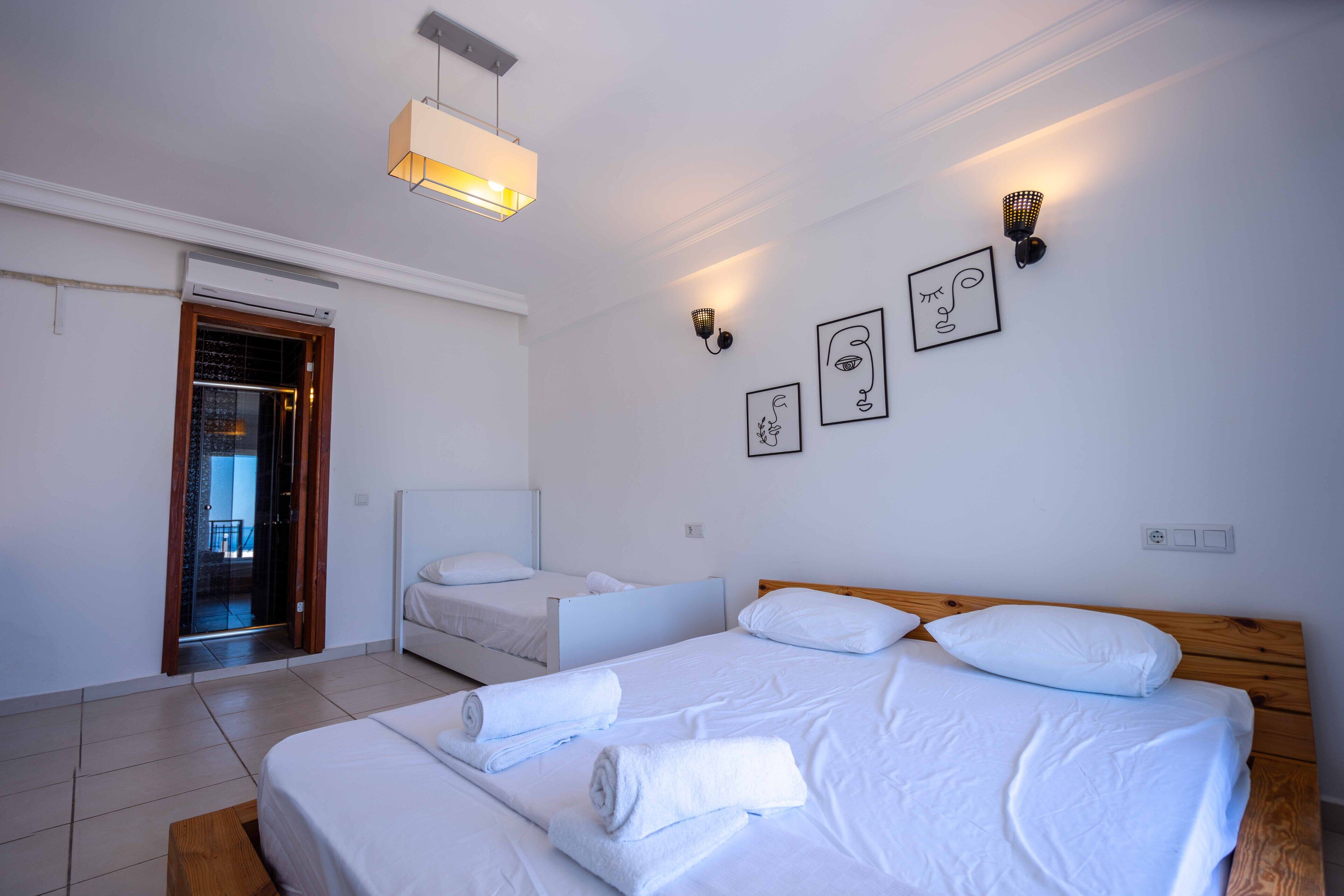 Une chambre d’hôtel avec deux lits, une tête de lit en bois, du linge de lit blanc, un banc et des œuvres d’art accrochées au mur.