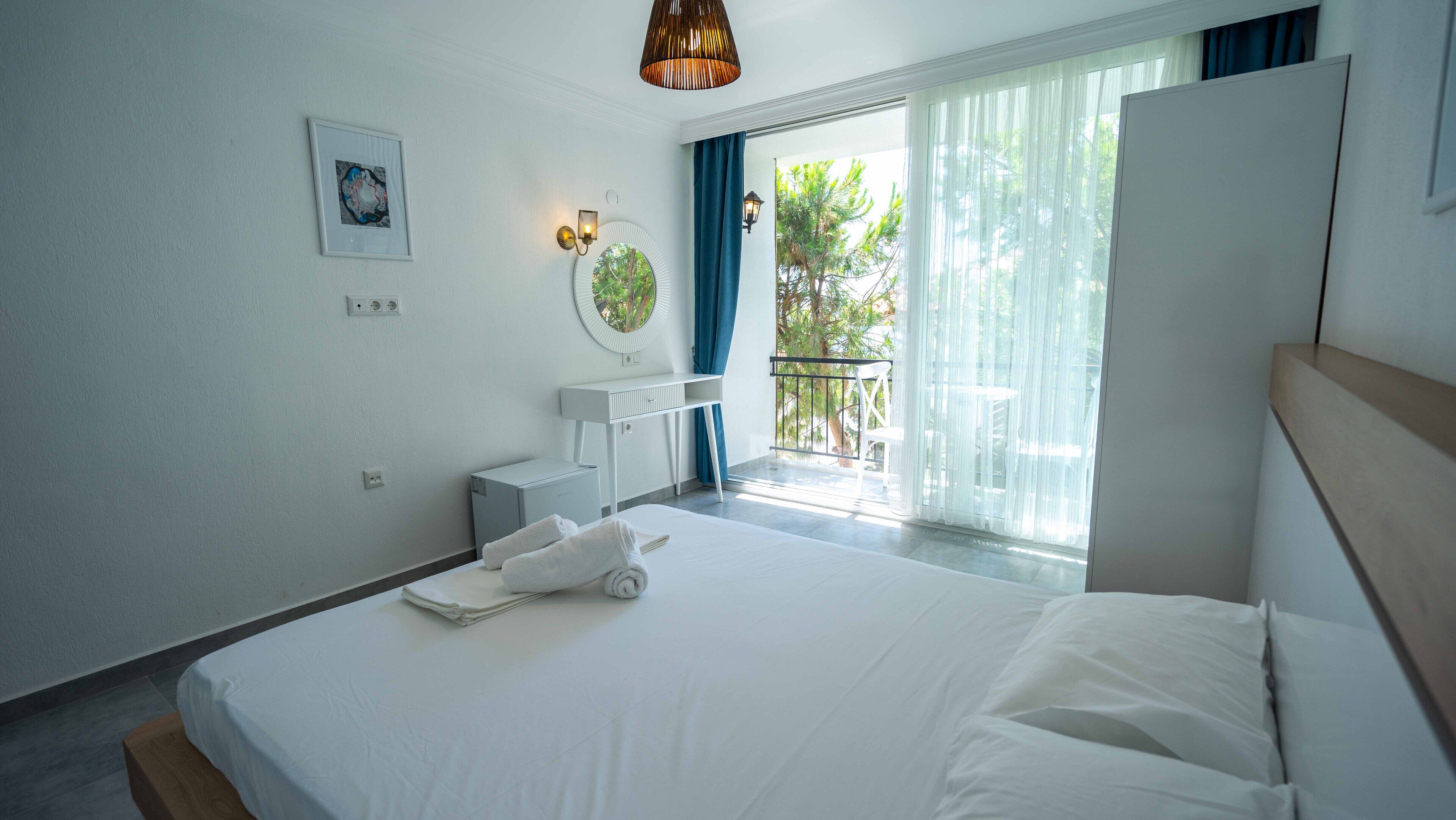 Habitación de hotel moderna con una cama grande, un escritorio pequeño, un espejo y un balcón con vistas a zonas verdes.