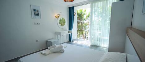 Habitación de hotel moderna con una cama grande, un escritorio pequeño, un espejo y un balcón con vistas a zonas verdes.