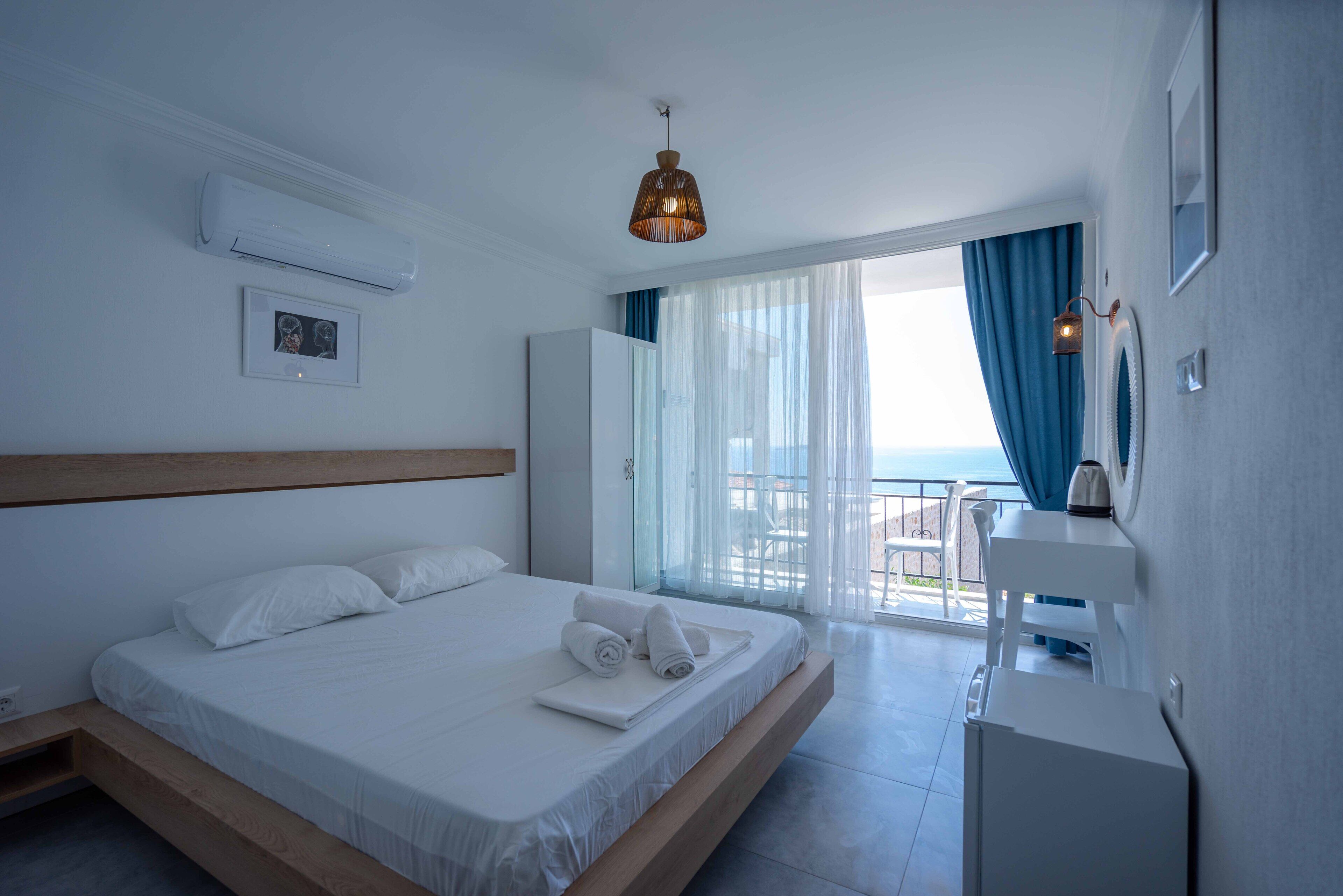 Habitación de hotel moderna con una cama grande, un escritorio pequeño y vista al mar desde el balcón.