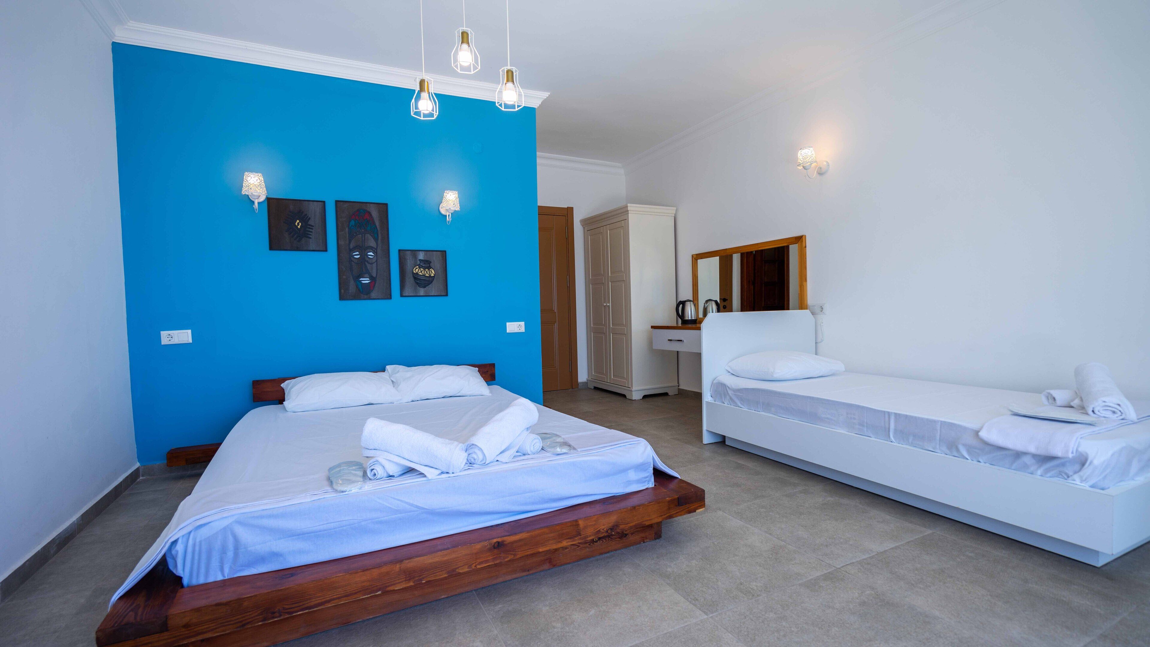 Una camera d'albergo con un letto grande, un letto più piccolo, un armadio, uno specchio e opere d'arte alle pareti.