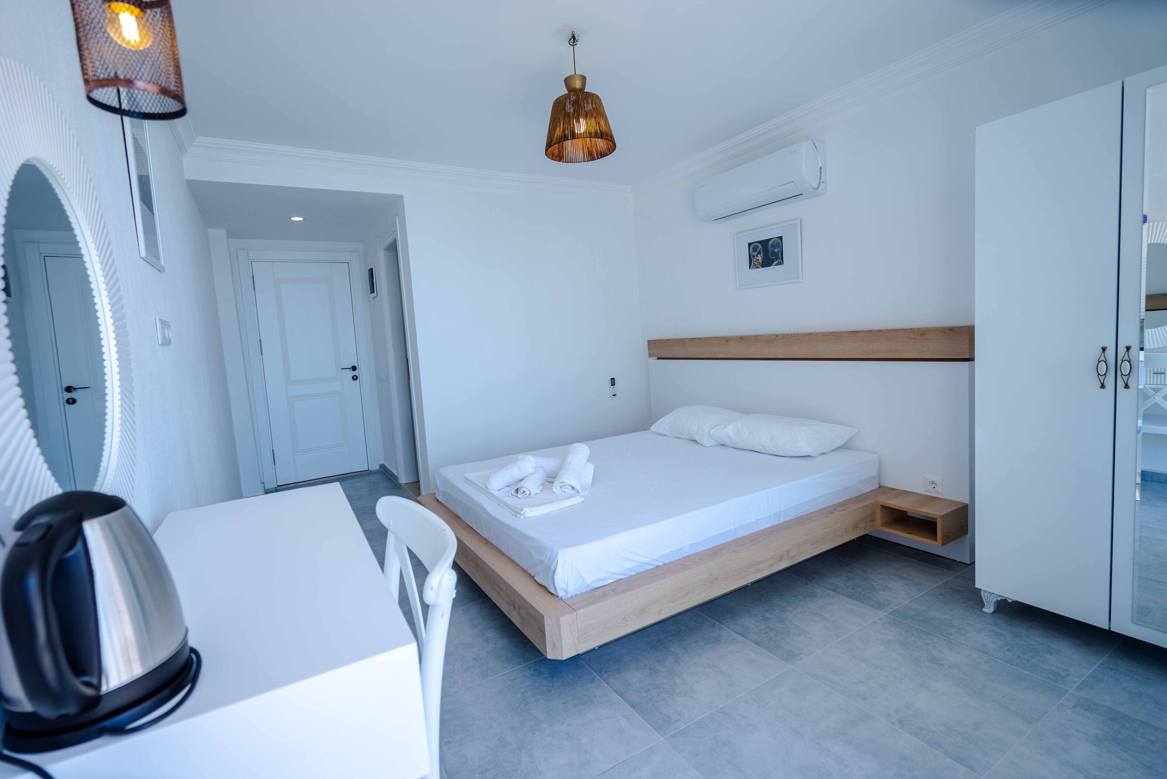 Een moderne hotelkamer met een houten bed, witte muren, een klein bureau met een waterkoker en een hanglamp.