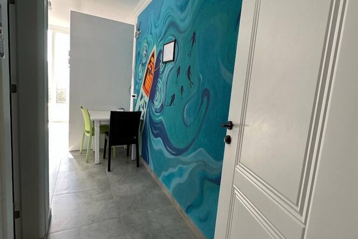 A hallway with a blue mural, a dining area with a table and chairs, and a white door.