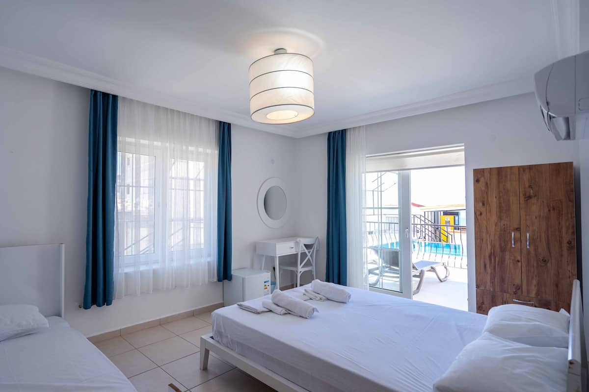 A hotel room with two beds, a large window with blue curtains, a round mirror, and a wooden wardrobe.