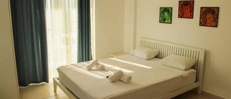 Una cama bien hecha con sábanas blancas, cabecera blanca y aire acondicionado instalado en la pared.