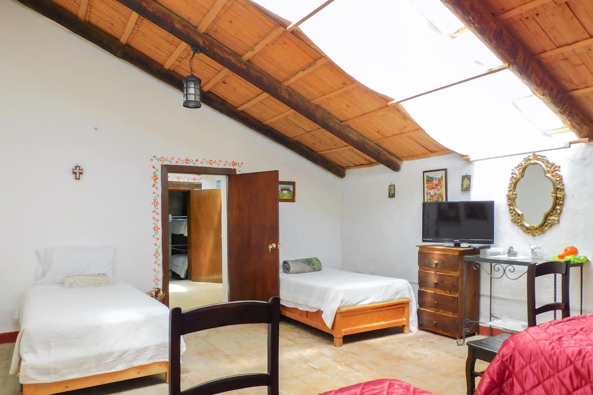 Una habitación con dos camas, televisión, espejo y techo de madera.