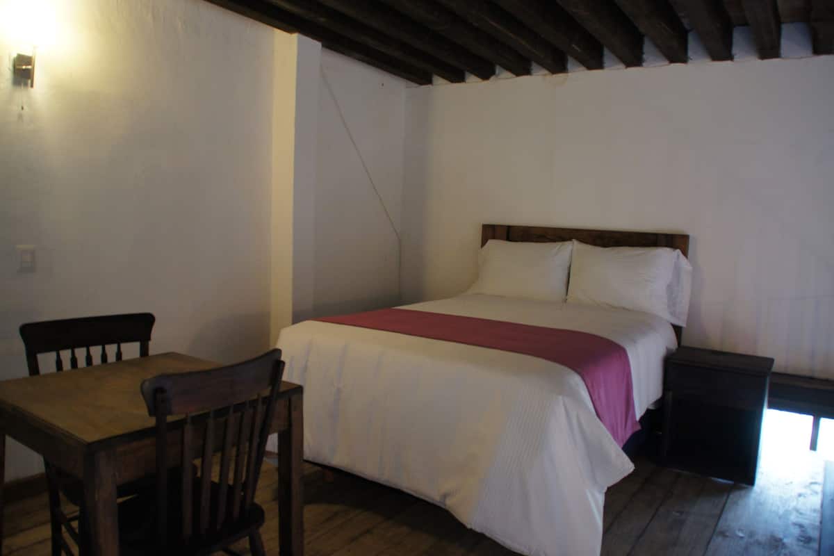 Una habitación pequeña y sencilla con una cama individual, una mesa de madera y una silla.