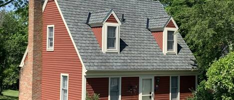 Una casa de dos pisos con fachada roja, una chimenea de ladrillo y un tejado gris.